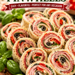 Italian Pinwheels served on a wooden platter with fresh basil, olives, and cherry tomatoes, easy make-ahead Italian party appetizer.
